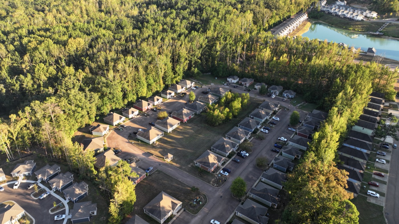 Golden-hour drone view of the Acadia Loop homes with the lake beyond the treeline, Oxford, MS