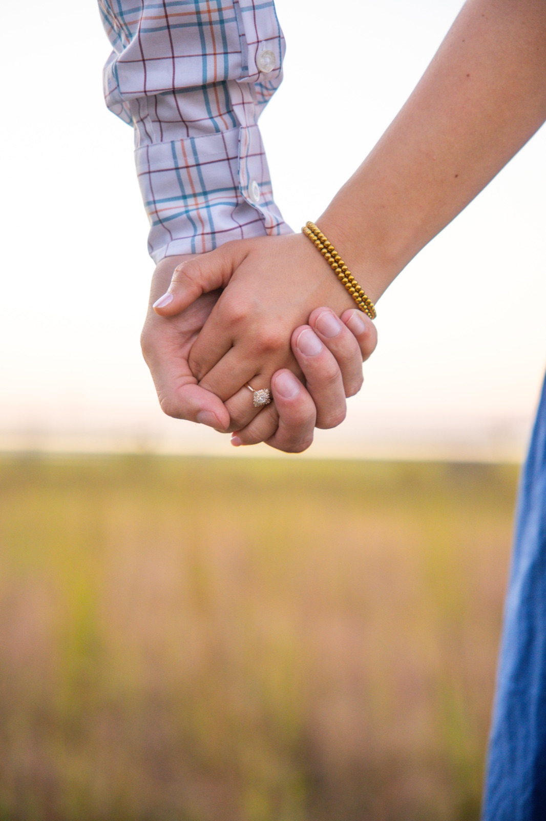 Engagement ring detail, hands held in a sunset field