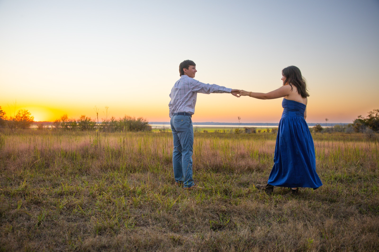 Engaged couple holding hands at arm's length against the sunset at Sardis Lake