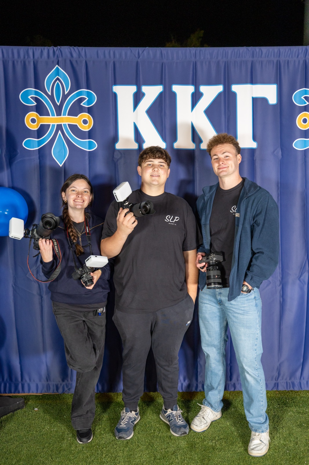 The SLP Media team, four photographers with cameras and lights, at the Kappa Kappa Gamma parents weekend backdrop