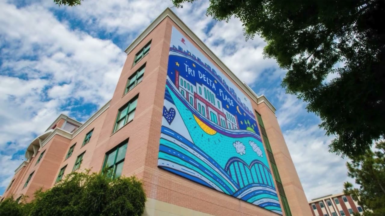 Frame from Tri Delta's Ole Miss philanthropy film, a brick building with a large Tri Delta Place mural under a blue sky