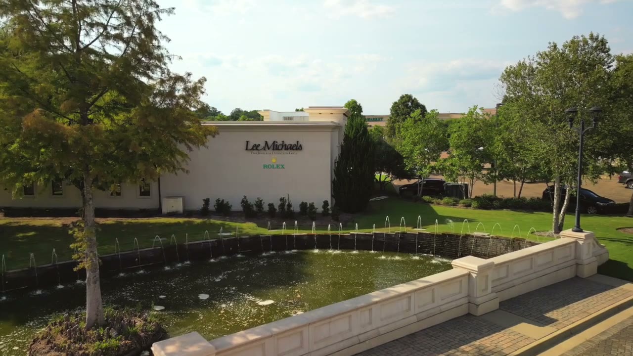 Frame from the Lee Michaels Fine Jewelry brand film: a white building with the Lee Michaels sign behind a fountain pond